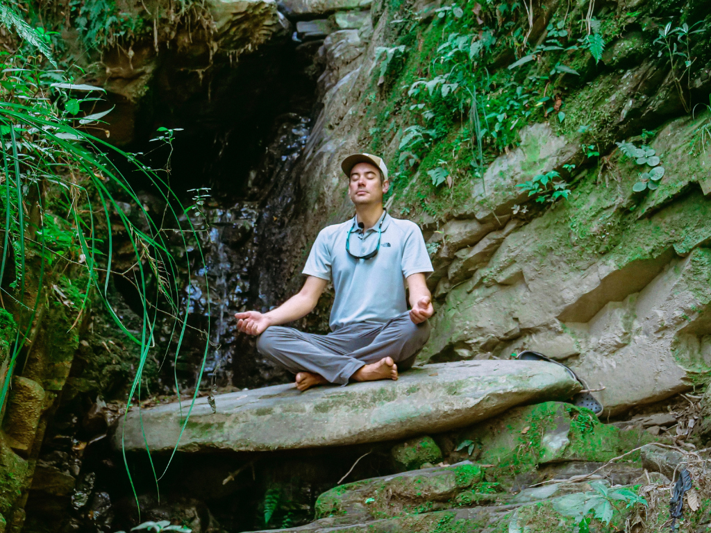A man performing Heartfulness meditation near a valley