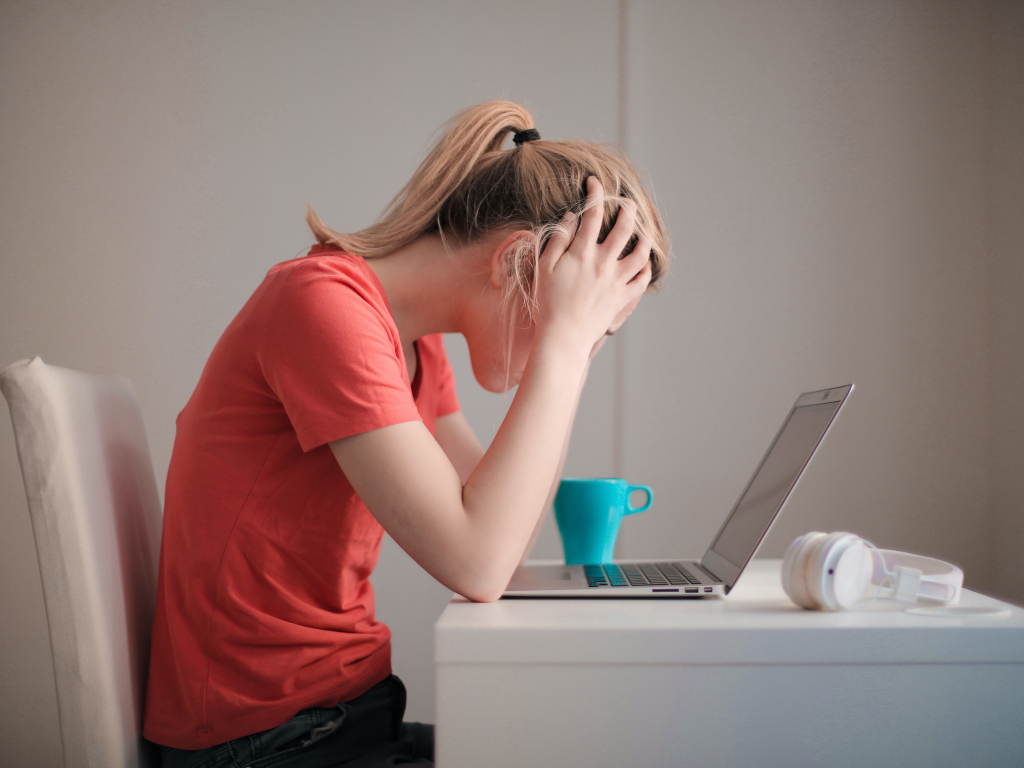 An image of a woman in a red t-shirt stressed looking at her laptop.
